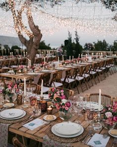 a table set up with place settings and candles for an outdoor wedding reception at dusk