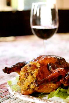 a roasted chicken on a plate next to a glass of wine