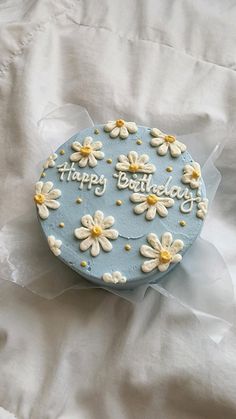 a birthday cake with daisies on it sitting on a white sheet covered tablecloth