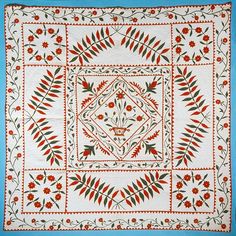 a white quilt with red flowers and leaves on the border, in front of a blue background