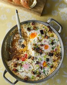 an omelet with eggs and vegetables in a pan on a table next to bread