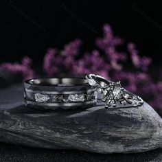 two wedding rings sitting on top of a rock with purple flowers in the back ground