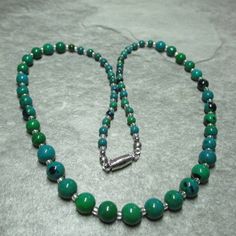 This graduated necklace features unusual Chrysocolla beads. At each end of the necklace are fifteen 4mm Chrysocolla beads, followed by eleven 6mm Chrysocollas and finally in the middle of the necklace eleven 8mm beads. All these Chrysocolla beads are separated by silver lined clear Glass seed beads. All the metal work is Stainless Steel including the magnetic clasp and the earwires on the free matching earrings. Necklace and earring come enclosed within a dark brown fine Velvet bag. Chrysocolla is a greenish/blue mineral of hydrated copper silicate. Is both refreshing and rejuvenating. During the Renaissance it was ground into powder to make pigment for paint. It's soothing properties guides to a state of calm and confidence. It is a stone of communications and of empowerment of the femini Green Chrysocolla Beaded Necklaces With Round Beads, Green Chrysocolla Beaded Necklaces, Green Chrysocolla Round Bead Necklaces, Green Chrysocolla Single Strand Necklace, Green Chrysocolla Round Beads Necklace, Jade Bead Necklace, Graduation Necklace, 8mm Beads, Wire Necklace