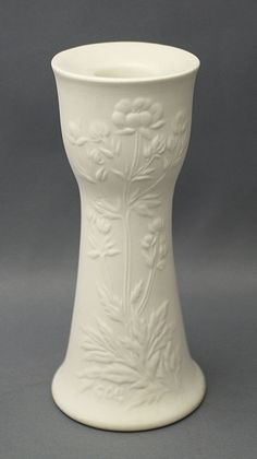 a white ceramic vase sitting on top of a table next to a gray wall and floor