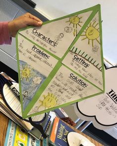 a person holding up a paper kite in front of a table with books and papers on it