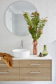 a bathroom with a sink and mirror next to a plant in a vase on the counter