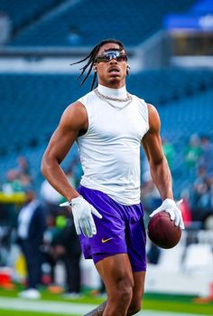 a man with dreadlocks holding a football on the field in front of a crowd