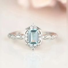 an engagement ring with a green emerald surrounded by white diamonds on a pink flower background