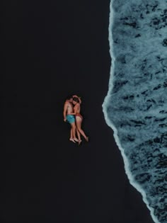 two people are laying on the beach in their bathing suits and swim trunks, one is holding his arm around the other's neck