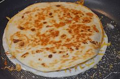 an uncooked tortilla sitting on top of a frying pan covered in cheese