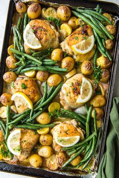 chicken, potatoes and green beans in a baking pan with lemons on the side