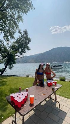 two women sitting at a picnic table with cups on it and one woman standing next to her