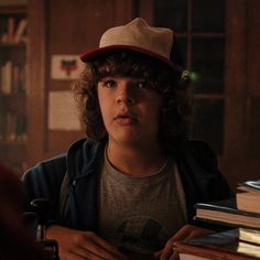 a young boy with curly hair wearing a hat sitting at a table full of books