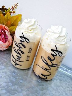 two iced coffees with whipped cream on them sitting next to a flower vase and some flowers