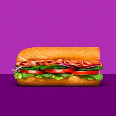 a large sandwich with meat, lettuce and tomato slices on it against a purple background