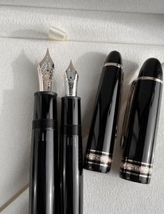 three fountain pens sitting next to each other on top of a white box with gold trim