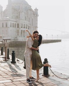 a man and woman are hugging by the water in front of a large white building