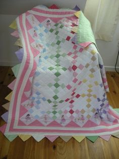 a pink and white quilt sitting on top of a wooden floor