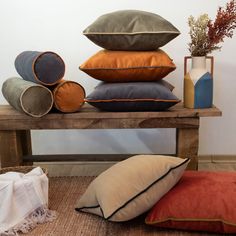 several pillows on a wooden table with vases and flowers in the corner behind them