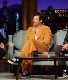 two men sitting on couches talking to each other in front of a tv screen