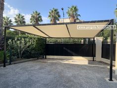 an empty parking lot with palm trees in the back ground and a large white awning over it