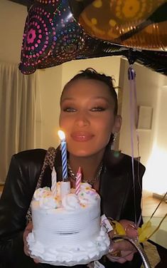 a woman holding a birthday cake with lit candles in her hand and balloons above her head