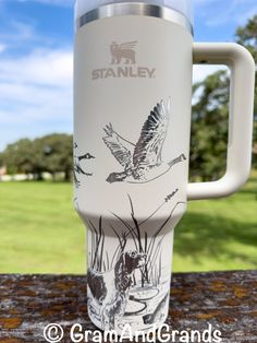 a white travel mug sitting on top of a wooden table next to a green field