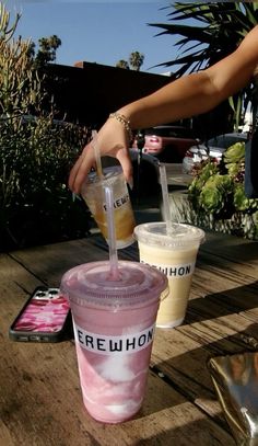 two drinks being poured into plastic cups with straws on the outside table in front of palm trees