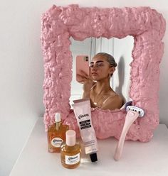 a woman taking a selfie in front of a pink mirror with makeup and hair products