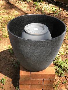 a black bowl sitting on top of a brick block in the middle of some grass