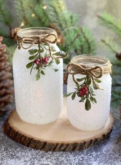 two mason jars decorated with holly and berries are sitting on a piece of wood next to pine cones