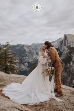 a bride and groom kissing on top of a mountain