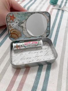 an open tin with some writing in it on a striped table cloth next to a person's hand