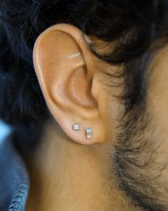 a close up of a person's ear with two square shaped earrings on it