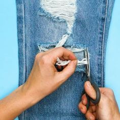 someone using scissors to cut through the hole in their jean pants that has been ripped