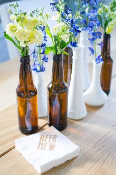 three beer bottles with flowers in them sitting on a table next to two napkins