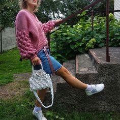 a woman in pink sweater and shorts sitting on steps holding a white purse with her legs crossed