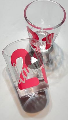 two shot glasses sitting next to each other on top of a white table with red lettering