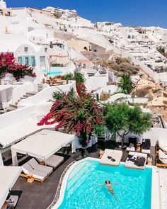 an outdoor swimming pool with lounge chairs and umbrellas next to the water in front of white buildings