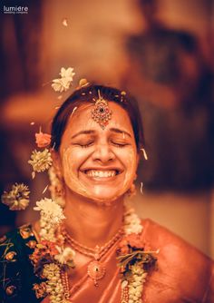 a woman smiling with flowers in her hair and jewelry around her neck, wearing an orange sari