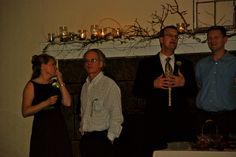 four people standing in front of a fireplace with candles on the mantel above them