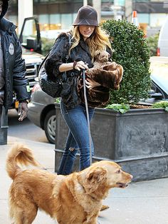 the woman is walking her dog down the street while wearing a hat and jacket with fur on it