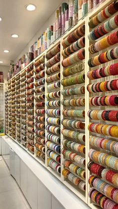 the wall is full of many different colored ribbons on it's sides, and there are several rows of brightly colored spools in each row