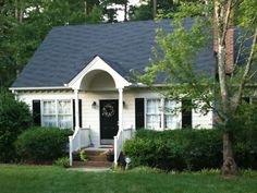 a white house with black shingles in the front yard