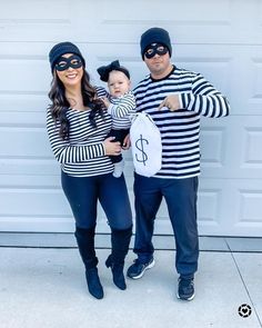 a man and woman dressed up as batman and catwoman with a baby in front of a garage door