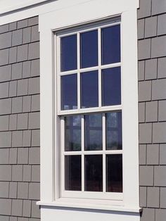 a black and white cat sitting on the ledge of a window sill in front of a gray house