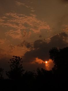 the sun is setting behind some clouds in the evening sky with trees silhouetted against it