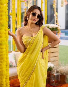 Bask in radiant elegance with this sunshine yellow georgette pre-draped sari ensemble! Effortlessly chic, the sari features intricate draping for a seamless look. The hand-embroidered bustier steals the spotlight with its dazzling embellishments of sequins, pearls, and cut-daana, complemented by delicate noodle straps. Embrace modern glamour with this captivating attire, perfect for making a statement at any special occasion. Haldi Outfits Saree, Haldi Saree Indian Bridal, Haldi Outfits For Bridesmaid, Yellow Outfits For Women, Yellow Saree For Haldi, Haldi Dresses, Haldi Saree, Haldi Bride, Yellow Sari