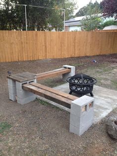 a concrete bench with a fire pit in the back ground next to a wooden fence