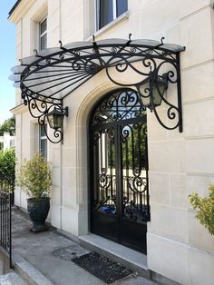 an iron gate is open on the side of a building with potted plants in front